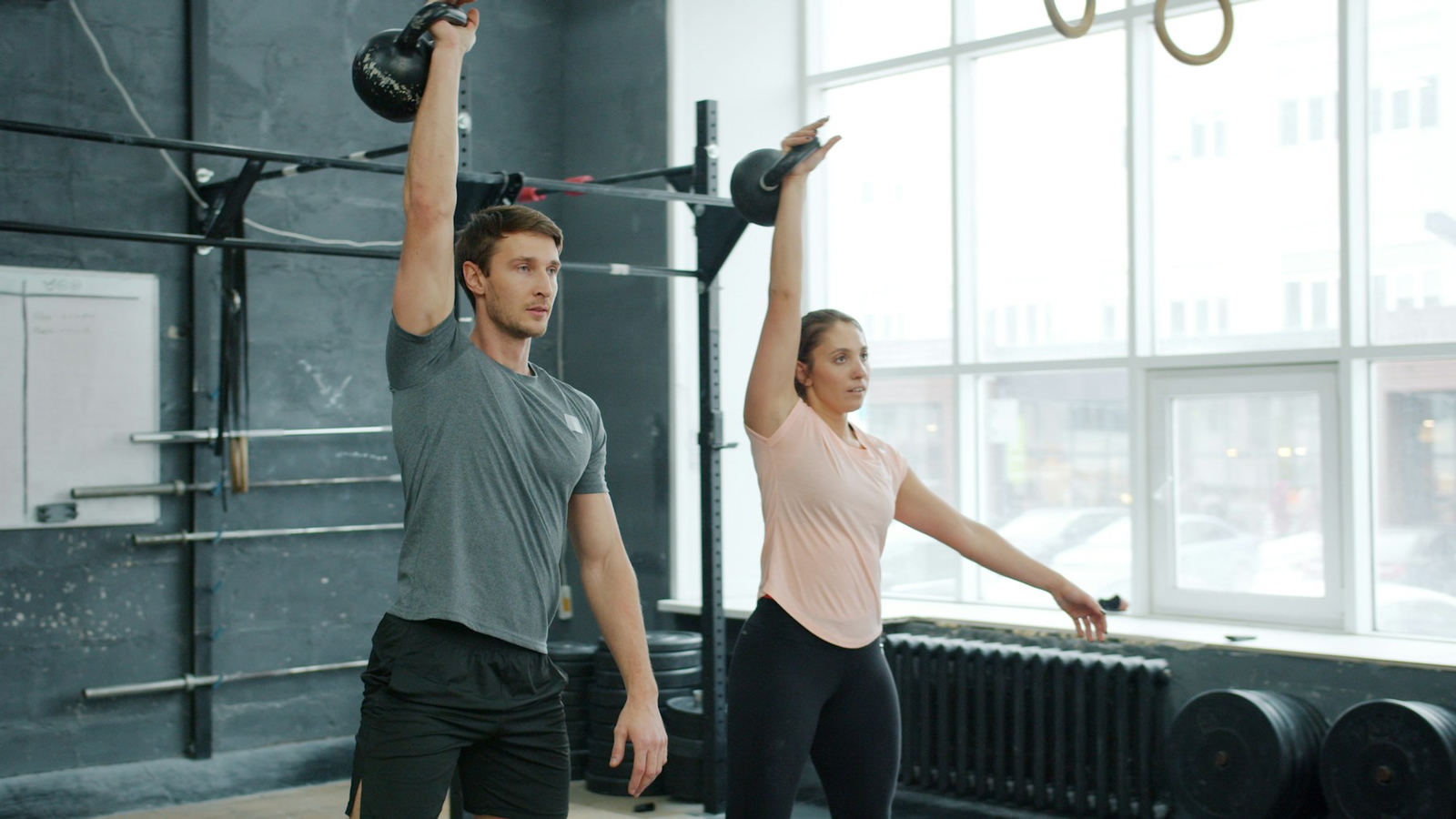 Two people pressing kettlebells overhead in a bright studio