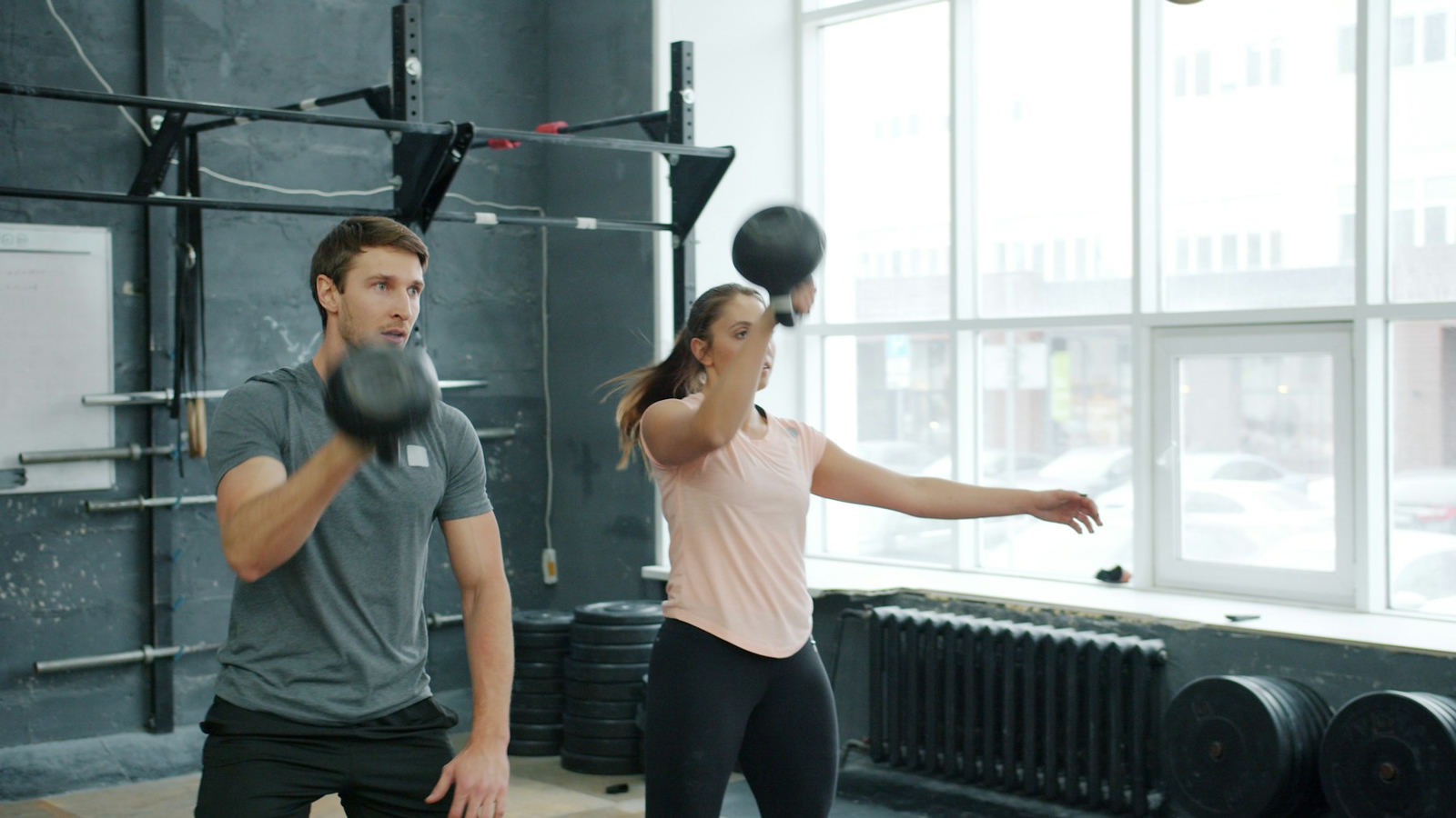 Two people squatting with kettlebells in a bright studio